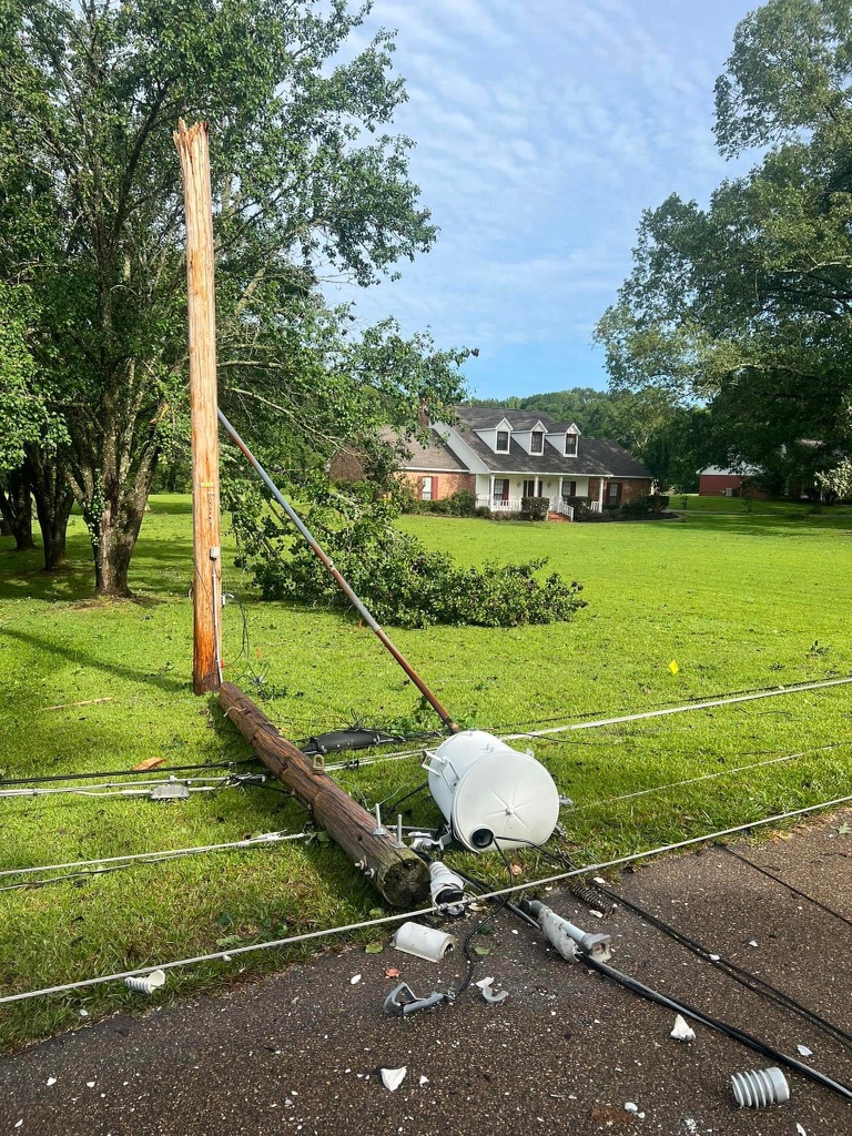A photograph depicting a telephone poll that has apparently snapped in half, the transformer having shattered to pieces and the power lines having been brought down.