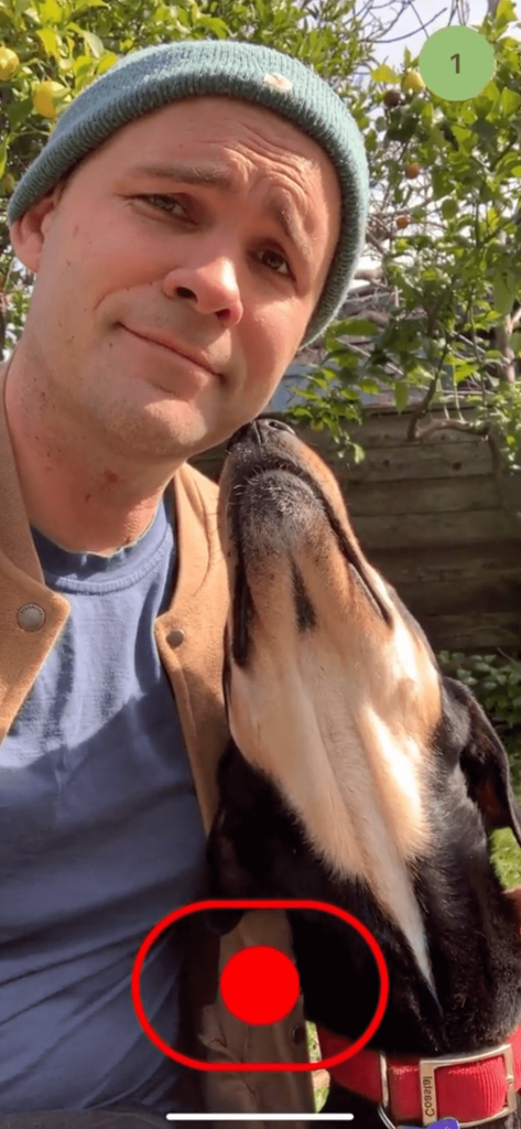 Screenshot of a video app in mobile portrait orientation. Shows Sloan smiling with his dog. A red record button is at the bottom.